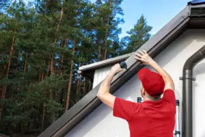 A roofing technician installs a gutter system on a residential property as part of a roofing project.